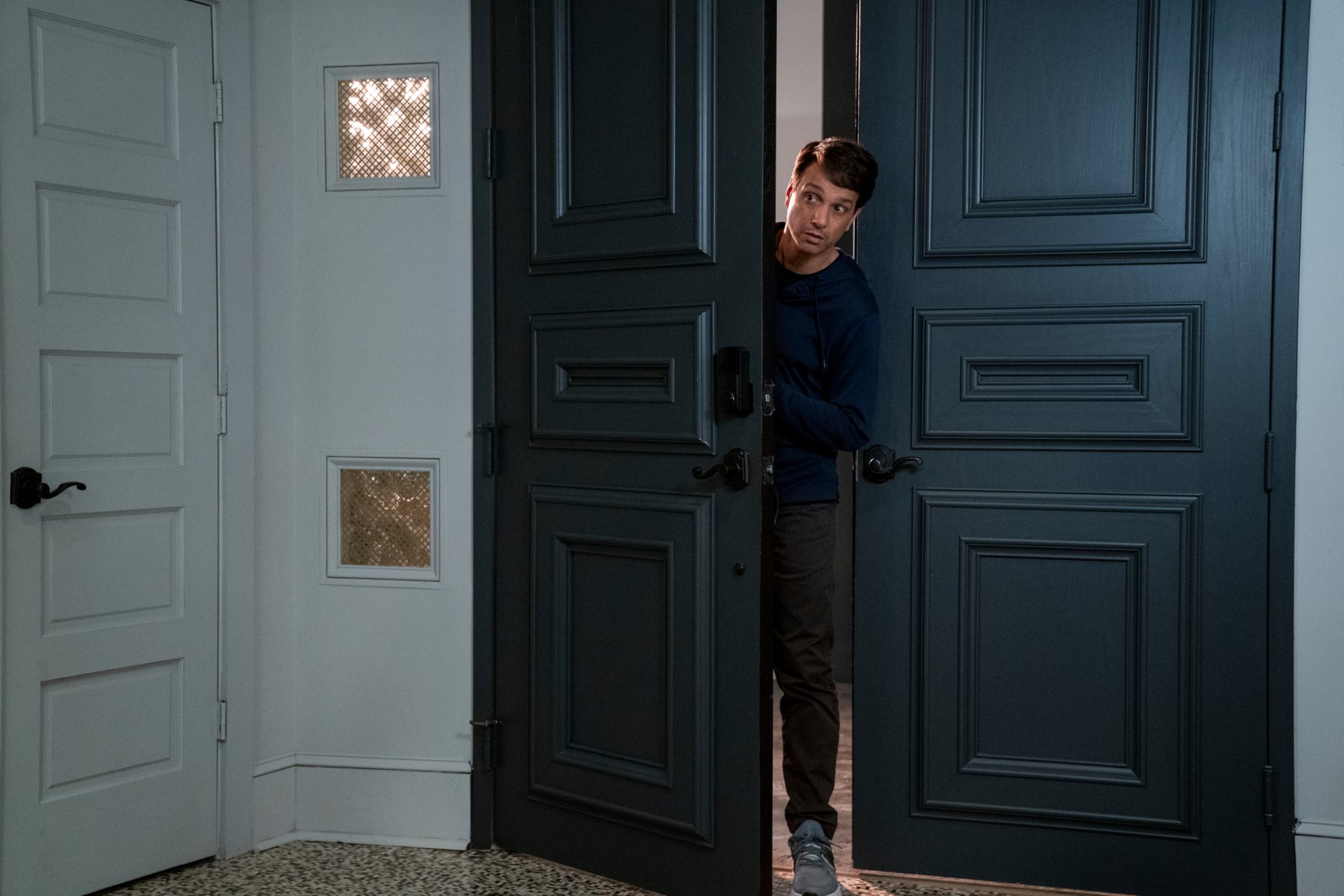 Cobra Kai TV show 2K Quad HD PC desktop wallpaper: a man peeks through tall double doors into a dim foyer, tense expression with dramatic, cinematic lighting.