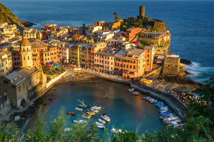 A vibrant 4K Ultra HD view of Vernazza in Cinque Terre showcasing colorful man-made buildings clustered around a serene harbor with boats and the deep blue sea.