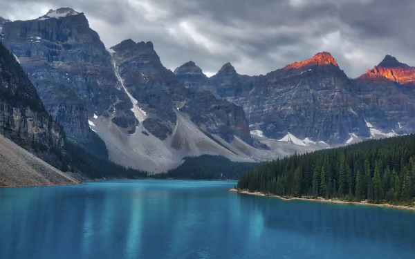 HD desktop wallpaper capturing the serene beauty of Moraine Lake, surrounded by rugged mountains and dense forest under a dramatic cloudy sky.