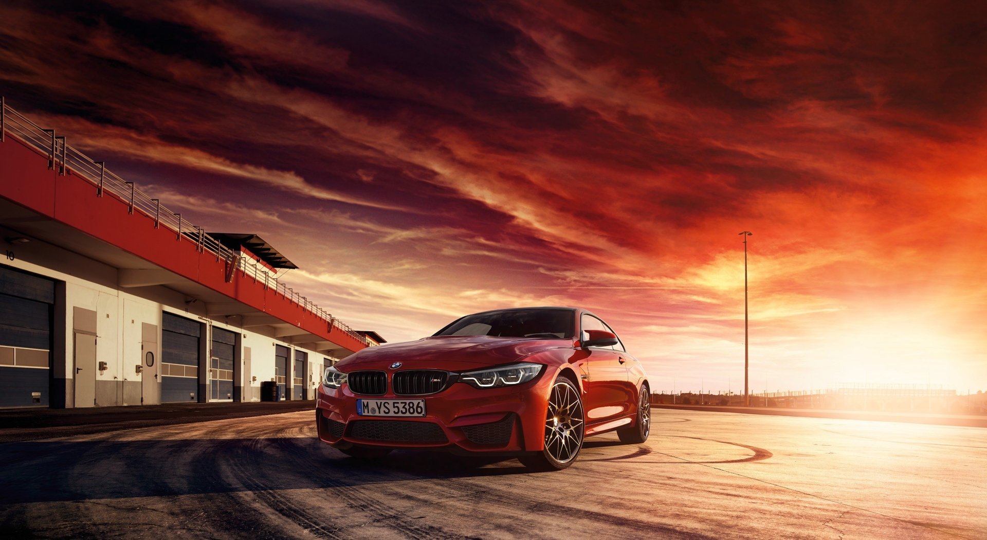 HD PC desktop wallpaper featuring a striking red BMW M4 parked on a racetrack under a dramatic sunset sky.
