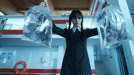 Jenna Ortega as Wednesday Addams from the TV show Wednesday holds two clear bags in a dark, high-definition PC desktop wallpaper background.