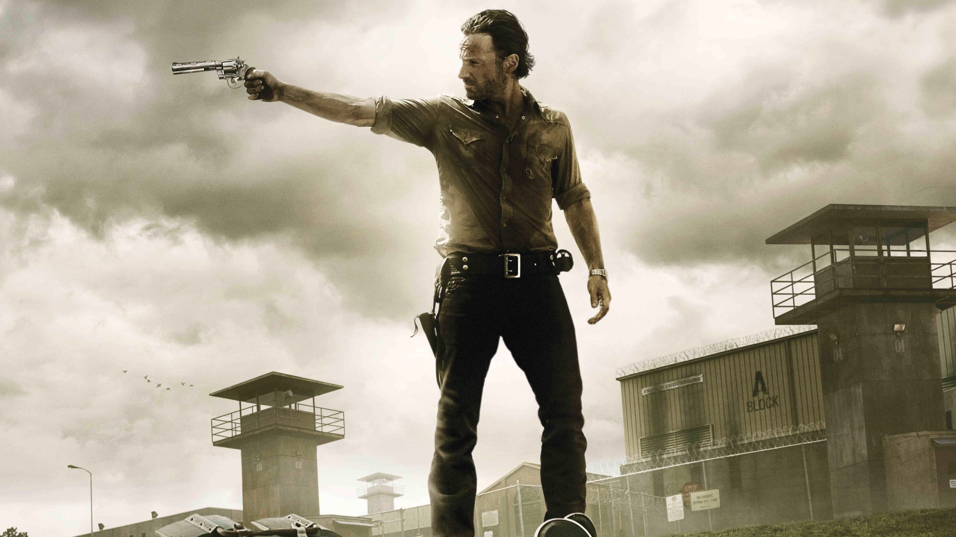 HD desktop wallpaper featuring a character from The Walking Dead TV show aiming a revolver, set against a cloudy sky and prison watchtowers in the background.