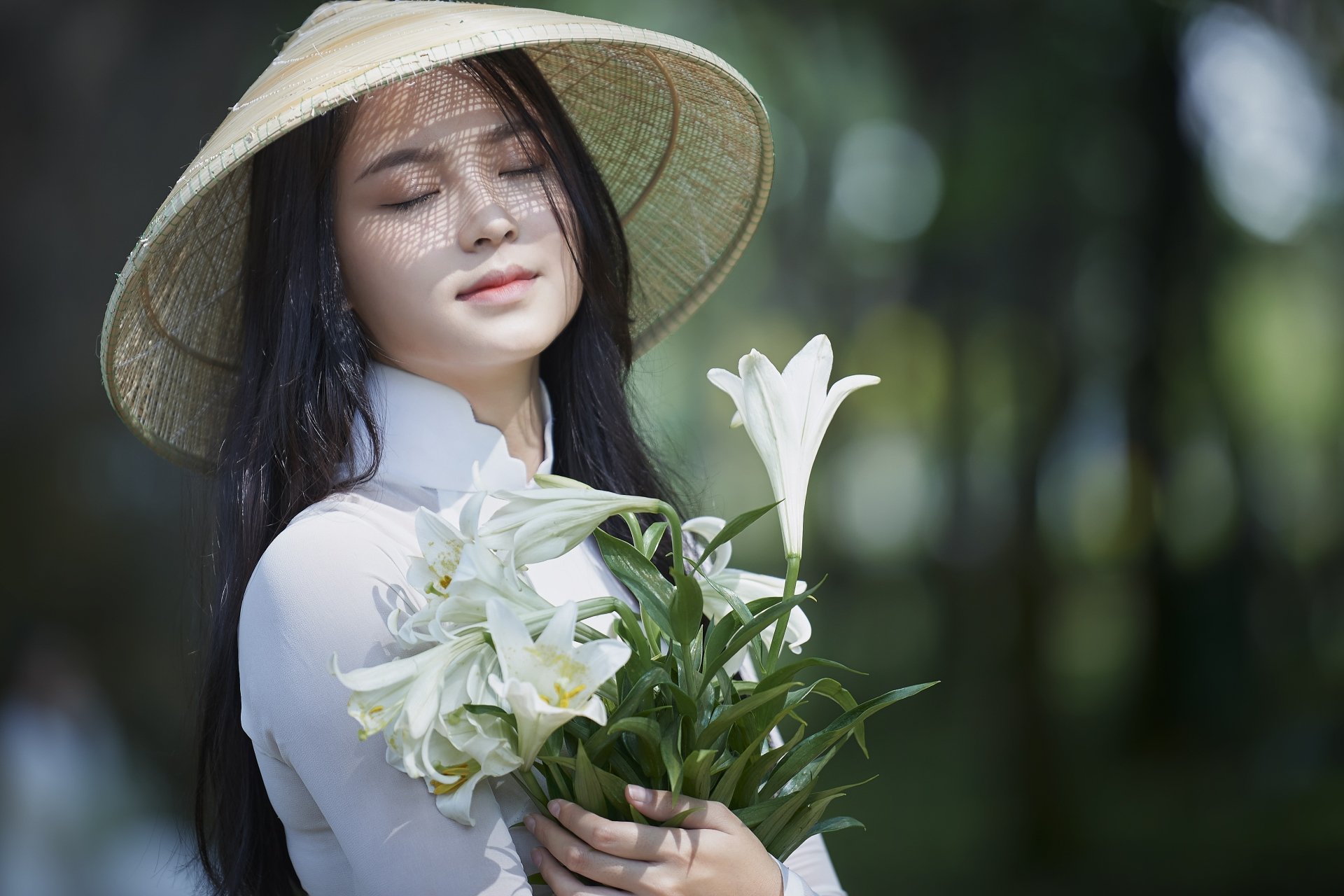4K Ultra HD PC desktop wallpaper: a woman in a conical hat gently cradles white lilies, eyes closed, against a soft-focus forest background.