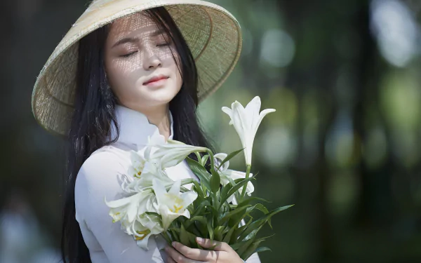 4K Ultra HD PC desktop wallpaper: a woman in a conical hat gently cradles white lilies, eyes closed, against a soft-focus forest background.