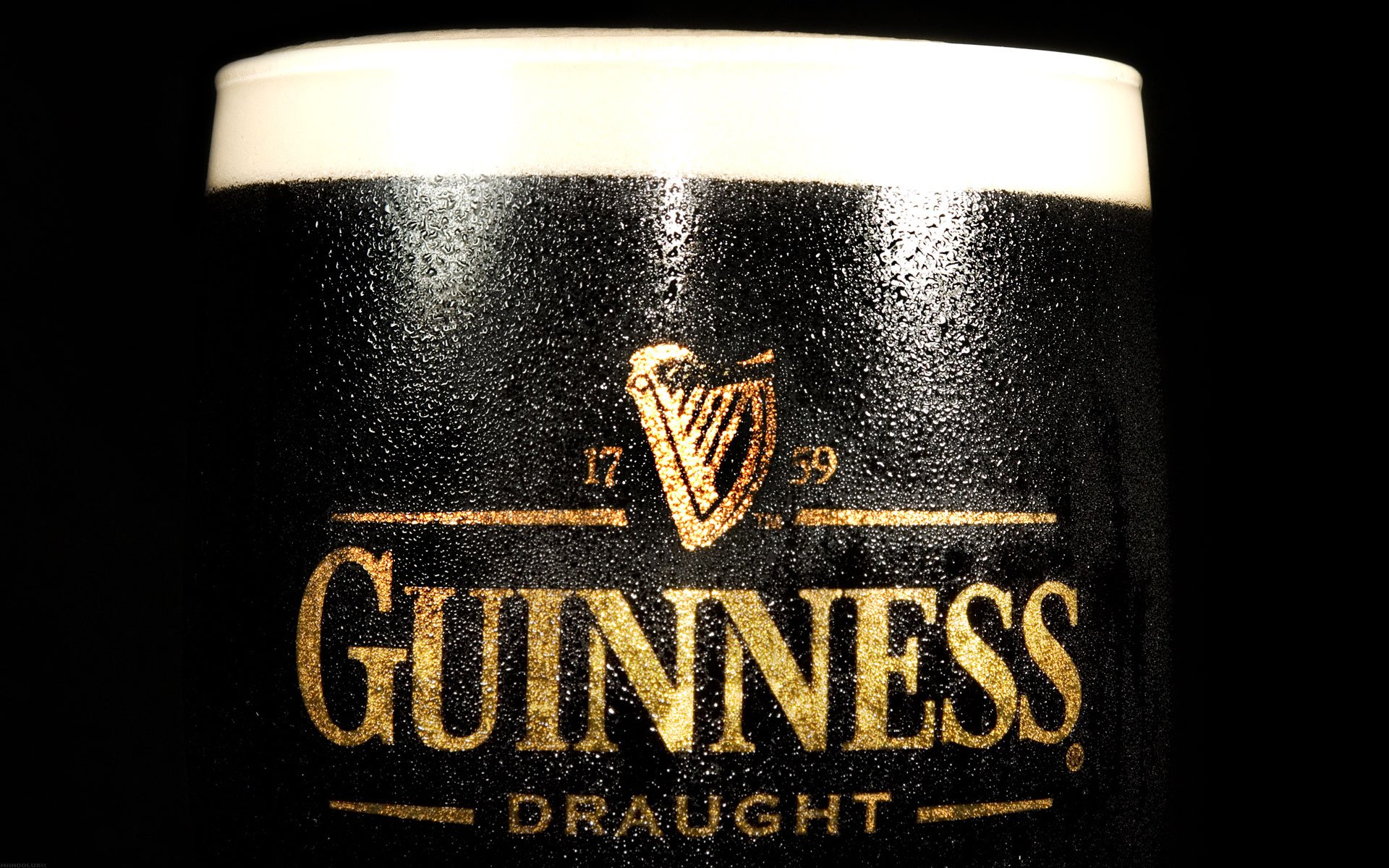 A close-up of a Guinness pint glass with elegant drops of condensation on a wooden countertop.
