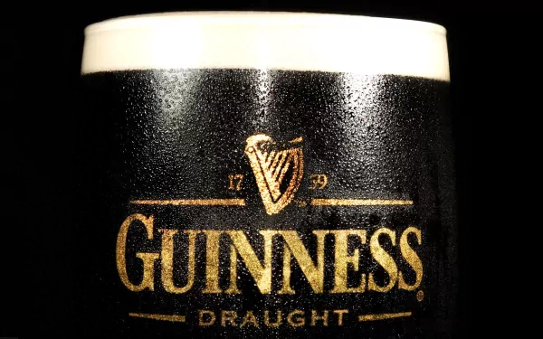 Close-up of a frosty pint of Guinness Draught, showcasing the iconic branding against a dark background. A striking HD wallpaper fit for beer enthusiasts.