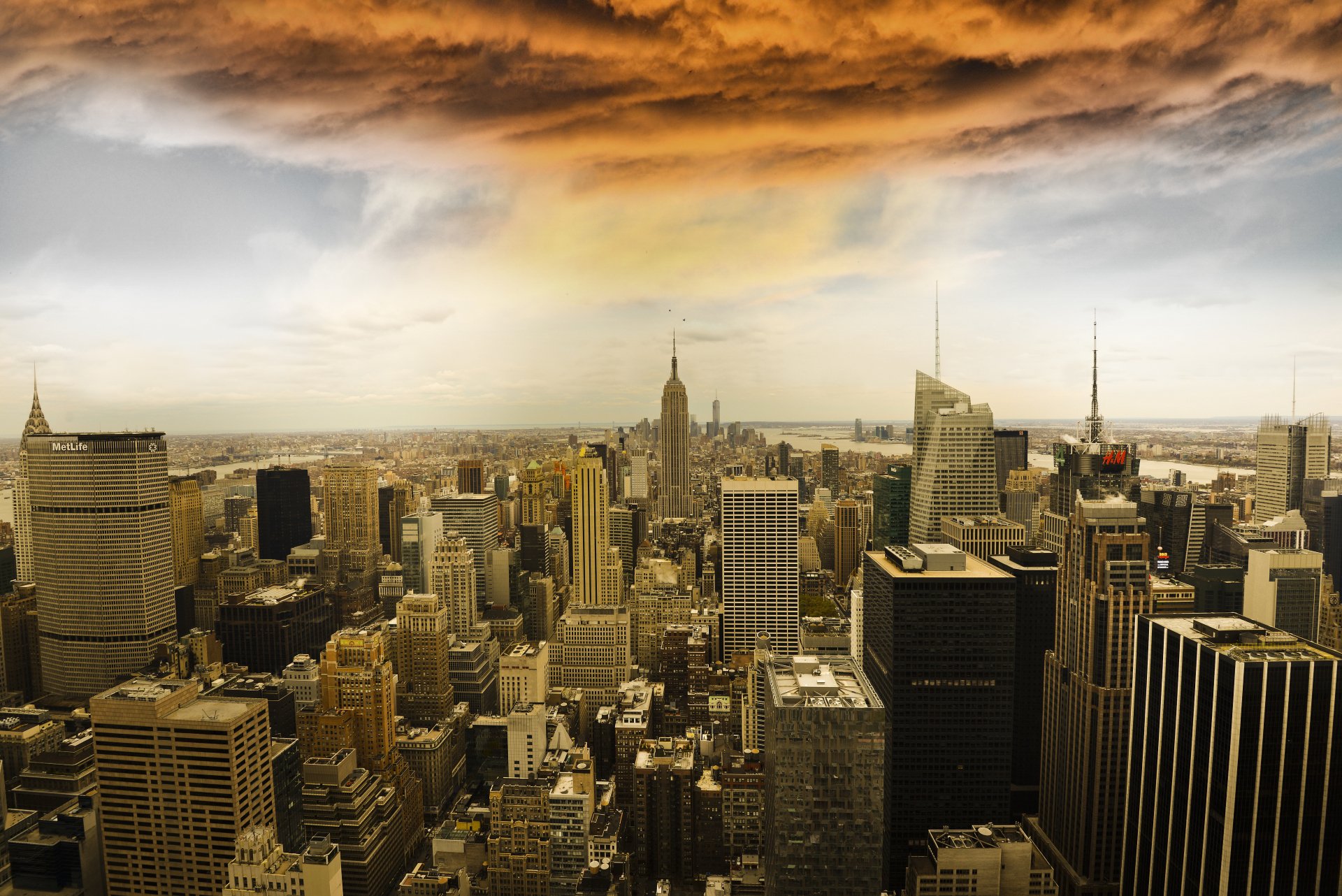 4K Ultra HD image of Manhattan's skyline featuring iconic skyscrapers under a dramatic, golden-orange sky, showcasing the man-made urban landscape.