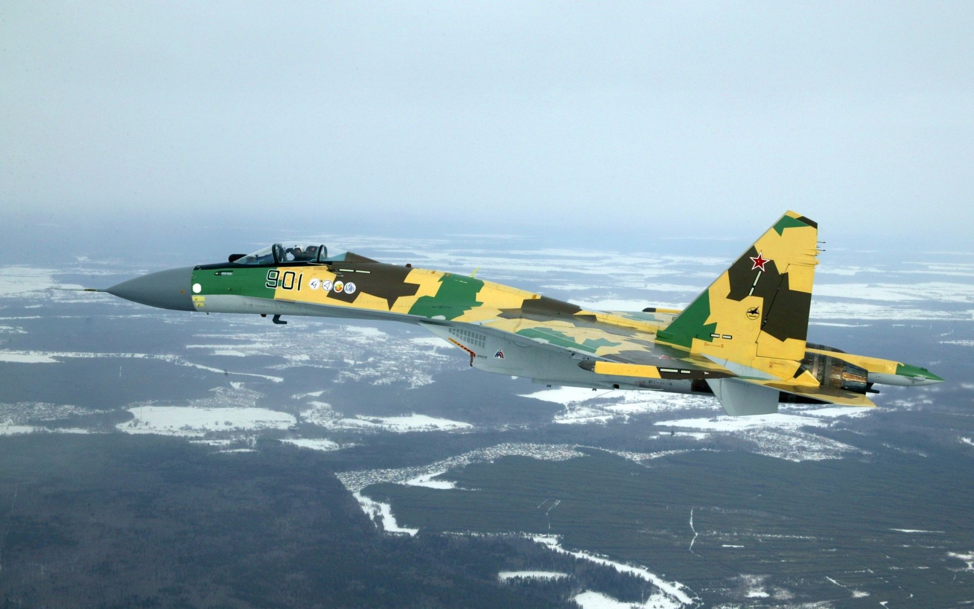 HD PC desktop wallpaper of a military Sukhoi Su-35 warplane in air force camouflage flying over a snowy landscape.