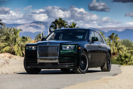 A sleek black Rolls-Royce Phantom parked on a desert road with palm trees and mountains under a partly cloudy sky in 4K Ultra HD quality.