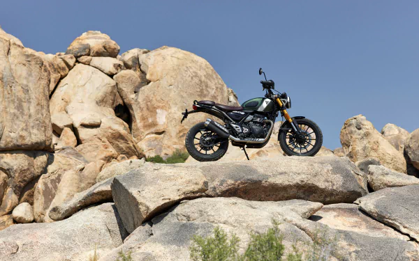 HD wallpaper of a Triumph Scrambler 400 X motorcycle perched on rocky terrain under clear blue skies.