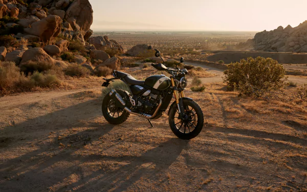 A Triumph Scrambler 400 X motorcycle parked on a dirt path, surrounded by rocky terrain and bathed in golden sunset light, creating a stunning HD wallpaper backdrop.