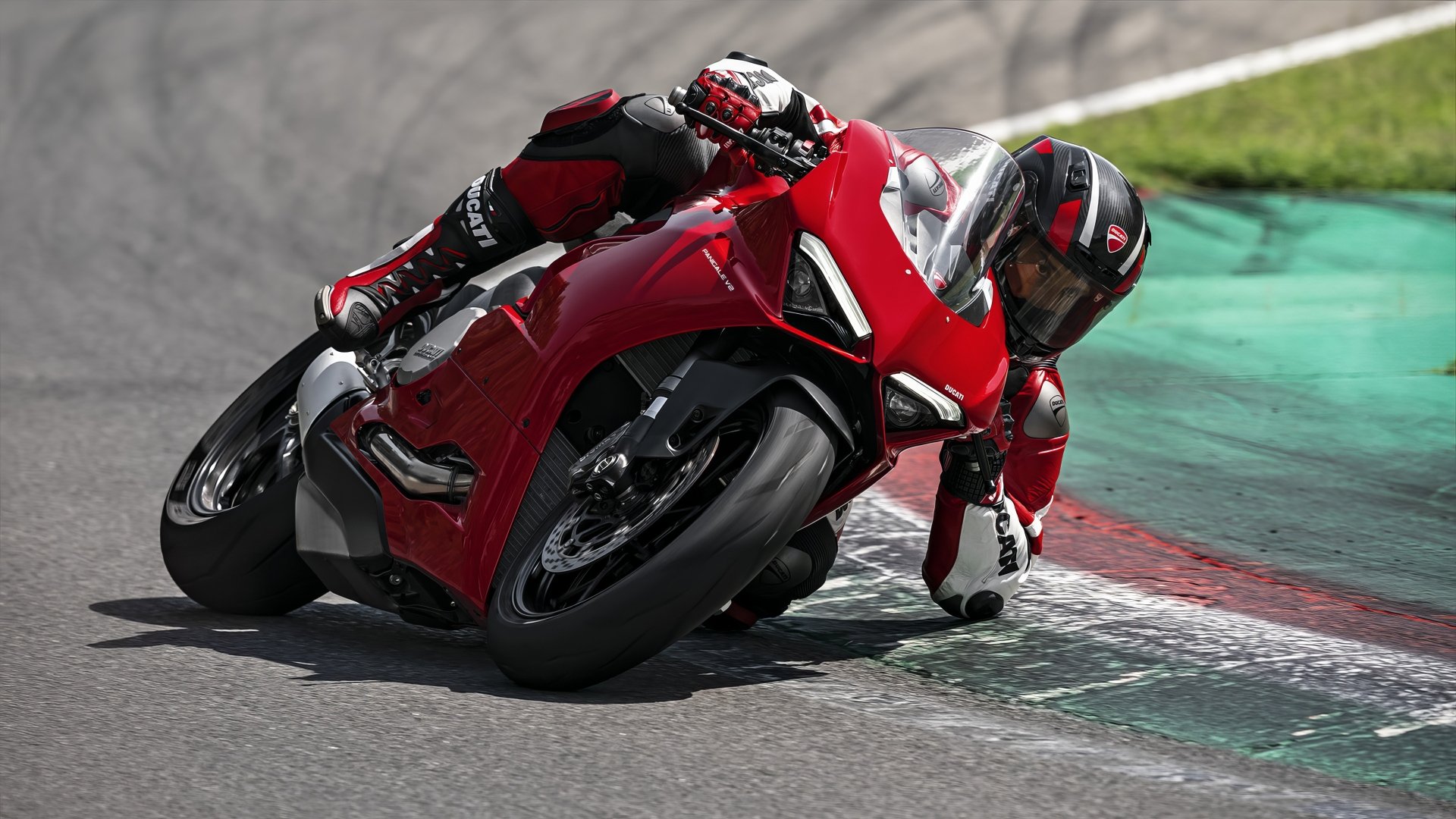 A rider leans into a curve on a Ducati Panigale V2, showcasing the motorcycle's sleek design and dynamic performance on the racetrack. HD desktop wallpaper and background.
