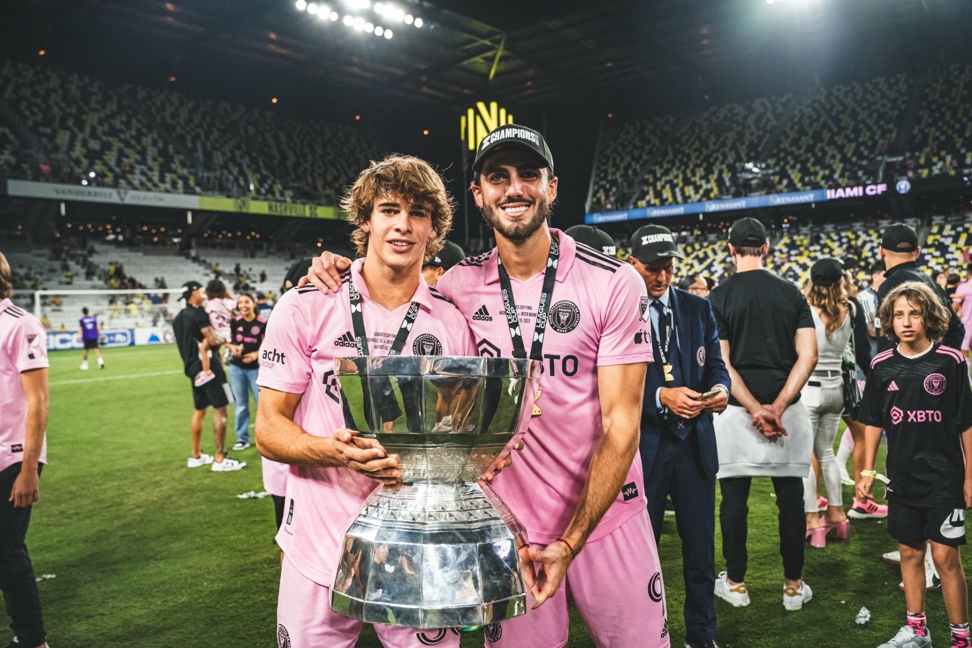 HD desktop wallpaper featuring two Inter Miami CF players celebrating with a trophy on the field, surrounded by fans in a packed stadium.