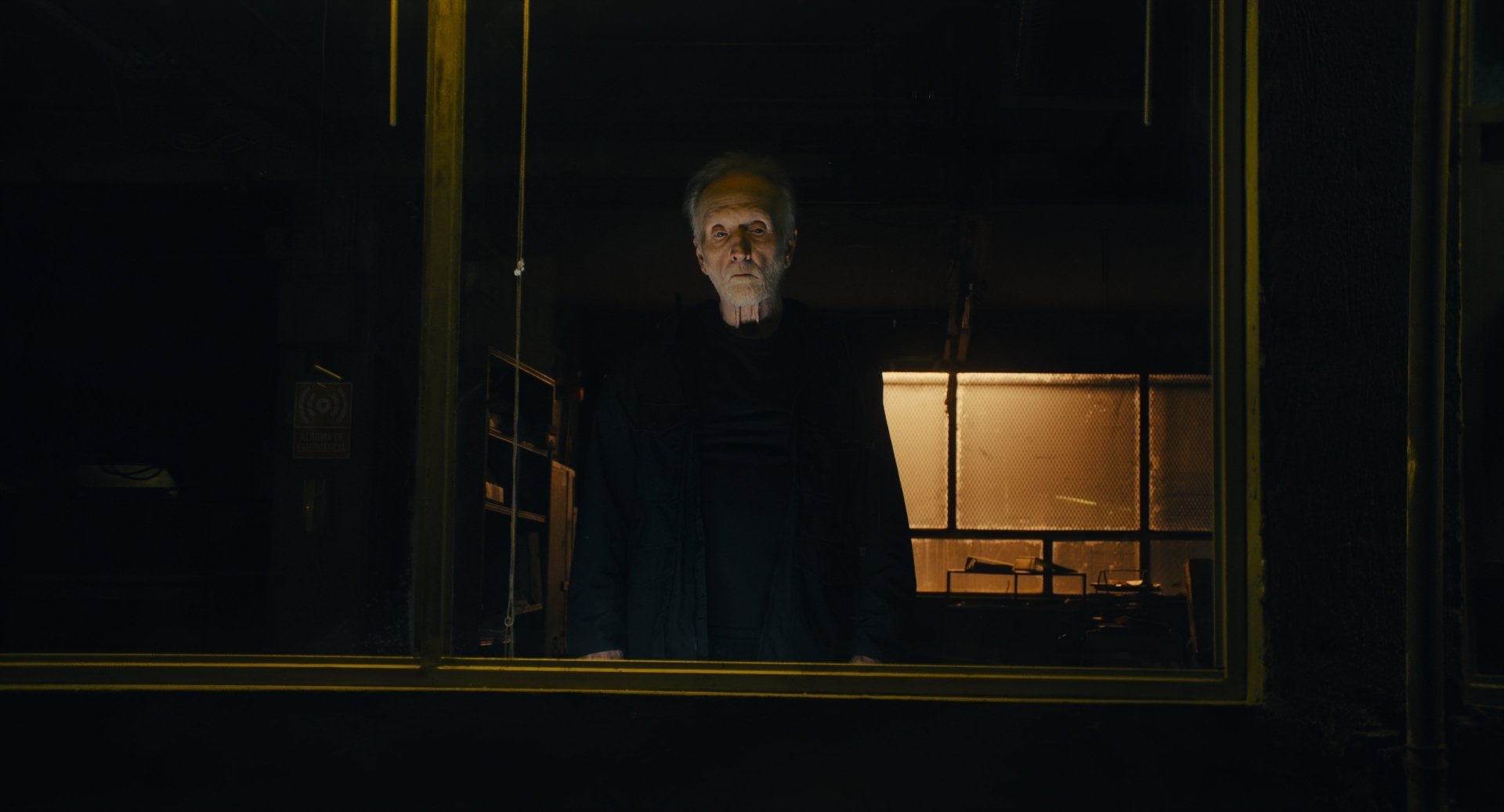 Tobin Bell stares intensely from a window in this HD desktop wallpaper for Saw X, capturing the film's dark and suspenseful atmosphere.