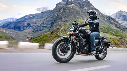 A rider on a Harley-Davidson X440 maneuvers along a scenic mountain road, showcasing the sleek design of this iconic motorcycle against a breathtaking backdrop.