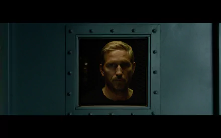 HD desktop wallpaper featuring a serious man looking through a ship's porthole, associated with the movie Sound of Freedom, evoking a mood of anticipation and solemnity.