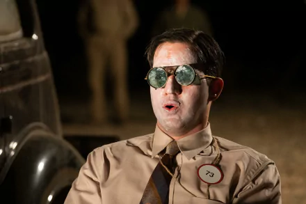 HD desktop wallpaper featuring a man in a vintage tan suit and sunglasses with an Oppenheimer tag, evoking a historical theme against a blurred background.
