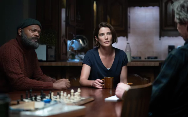 A dramatic scene from Secret Invasion, featuring three characters in a dimly lit kitchen, capturing an intense moment at the table with a chessboard in view.