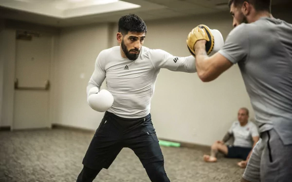 HD wallpaper of UFC fighter Ilia Topuria practicing punches with his trainer in a gym setting.