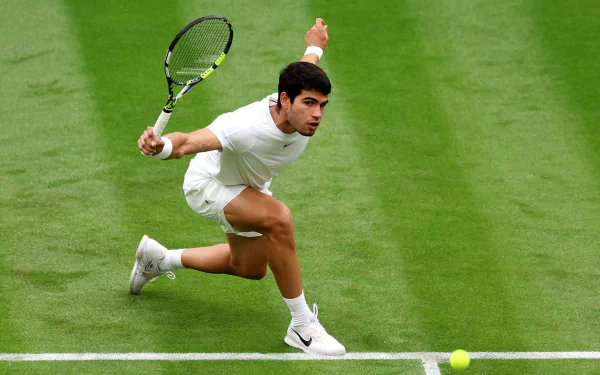 Carlos Alcaraz in action at Wimbledon 2023, showcasing his athleticism on the lush green court while poised to hit a tennis ball. A dynamic sports wallpaper capturing the excitement of tennis.