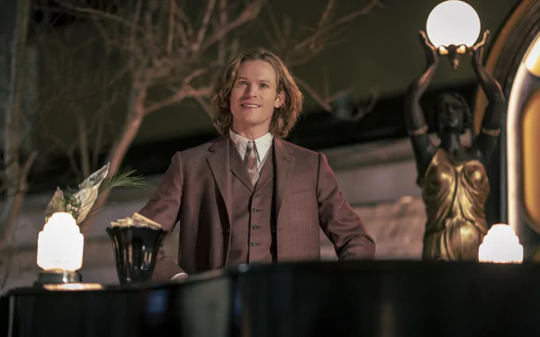HD wallpaper of Sam Reid from 'Interview with the Vampire', standing elegantly with vintage lamp posts in the background.