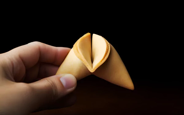 HD desktop wallpaper featuring a hand holding a fortune cookie against a dark background, highlighting the cookie's detail and texture.