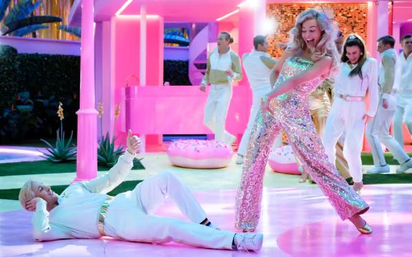HD wallpaper of two actors in a vibrant Barbie-themed setting, the woman in a sparkling pink outfit, the man in a white suit, with a whimsical, energetic vibe.