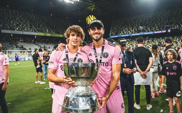 HD desktop wallpaper featuring two Inter Miami CF players celebrating with a trophy on the field, surrounded by fans in a packed stadium.