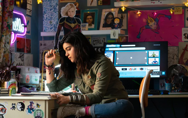HD desktop wallpaper featuring Iman Vellani in a scene from The Marvels, with vibrant superhero posters and neon lights.