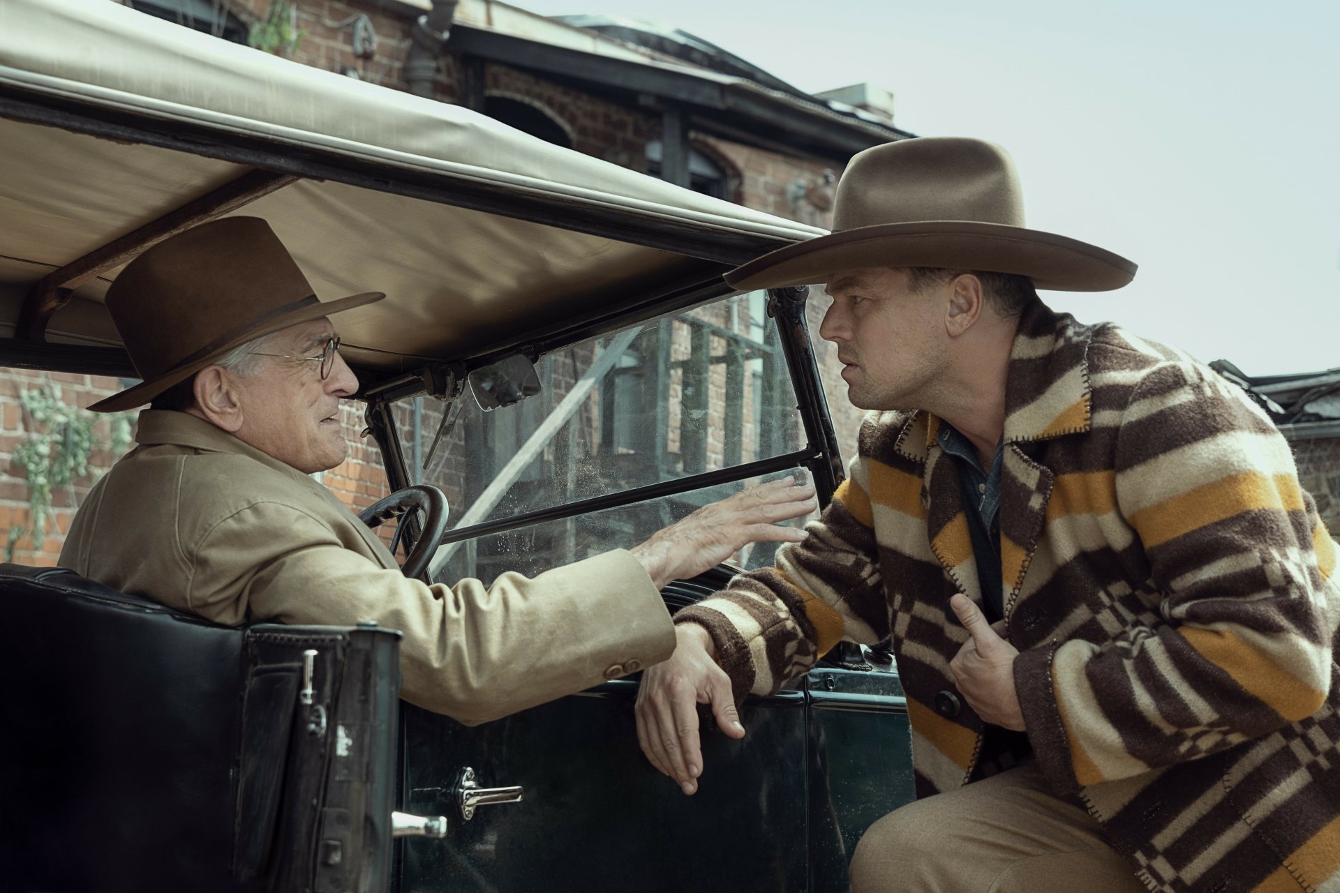 HD desktop wallpaper featuring two actors in period costumes, one seated in a vintage car and the other standing beside it, in a scene tagged with Killers of the Flower Moon.