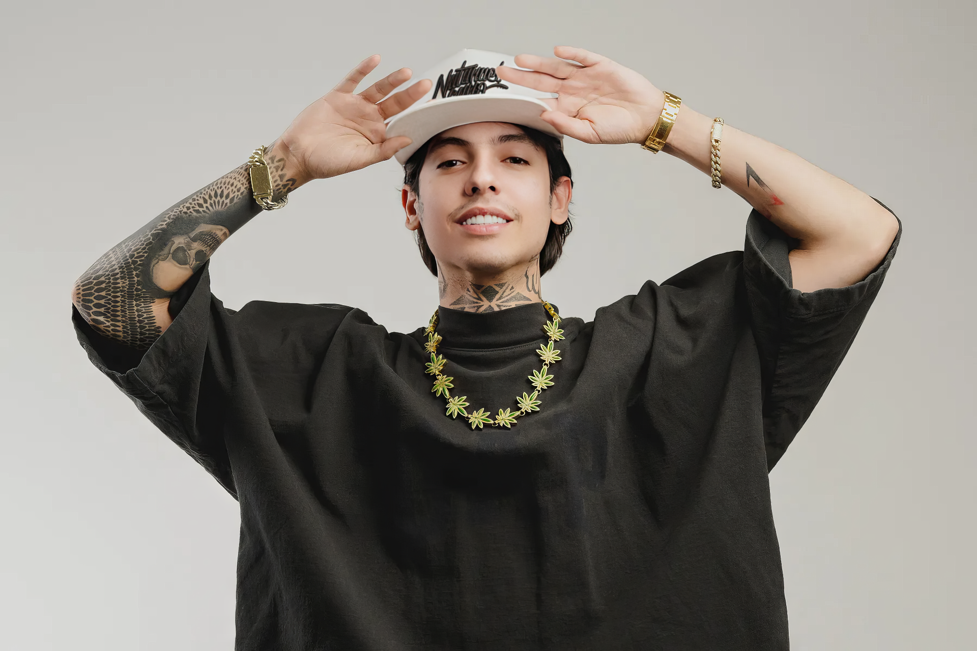 A trendy HD desktop wallpaper featuring Natanael Cano, showcasing his signature style with tattoos, a hat, and a statement necklace against a neutral background.