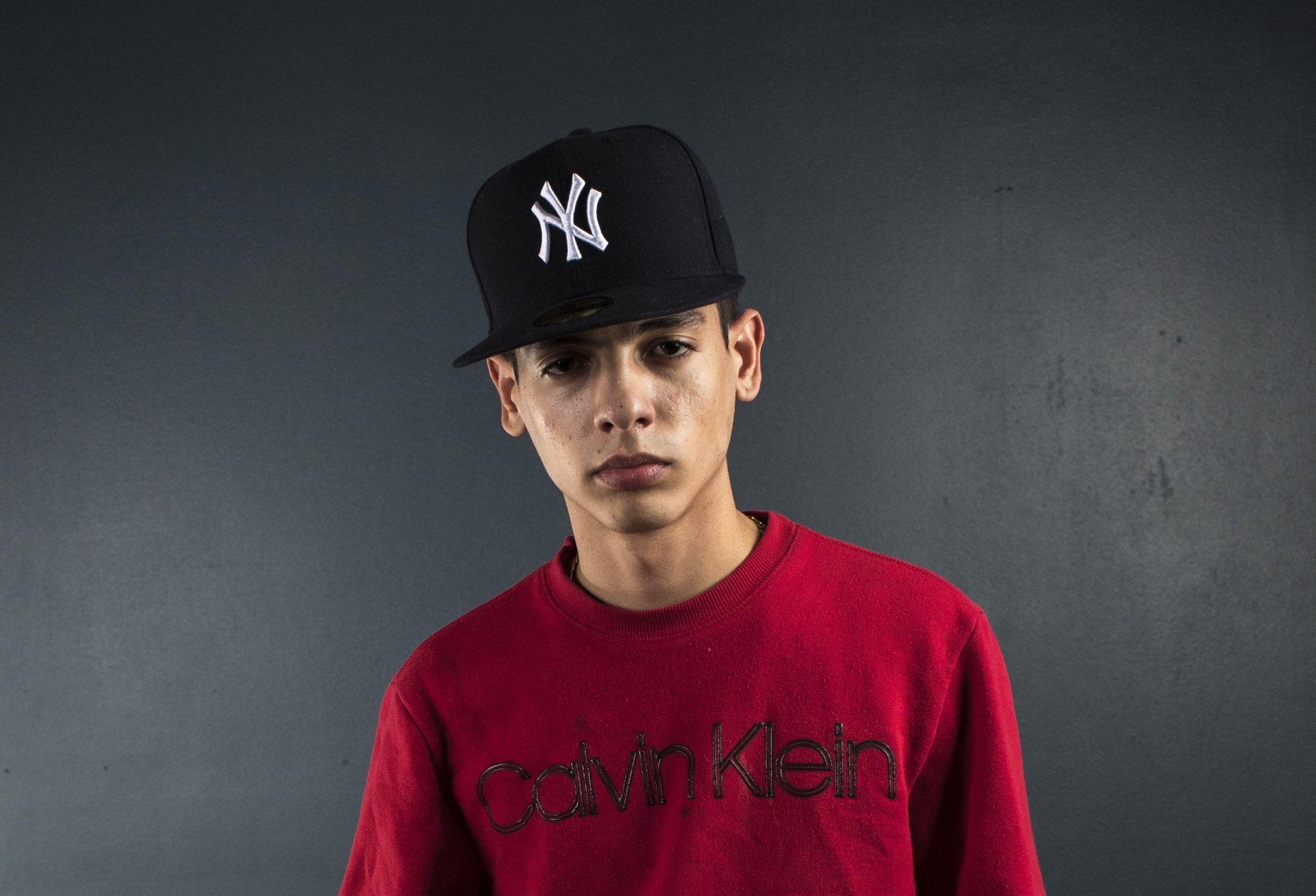 HD wallpaper of a person wearing a red shirt and a NY baseball cap on a grey background for desktop.