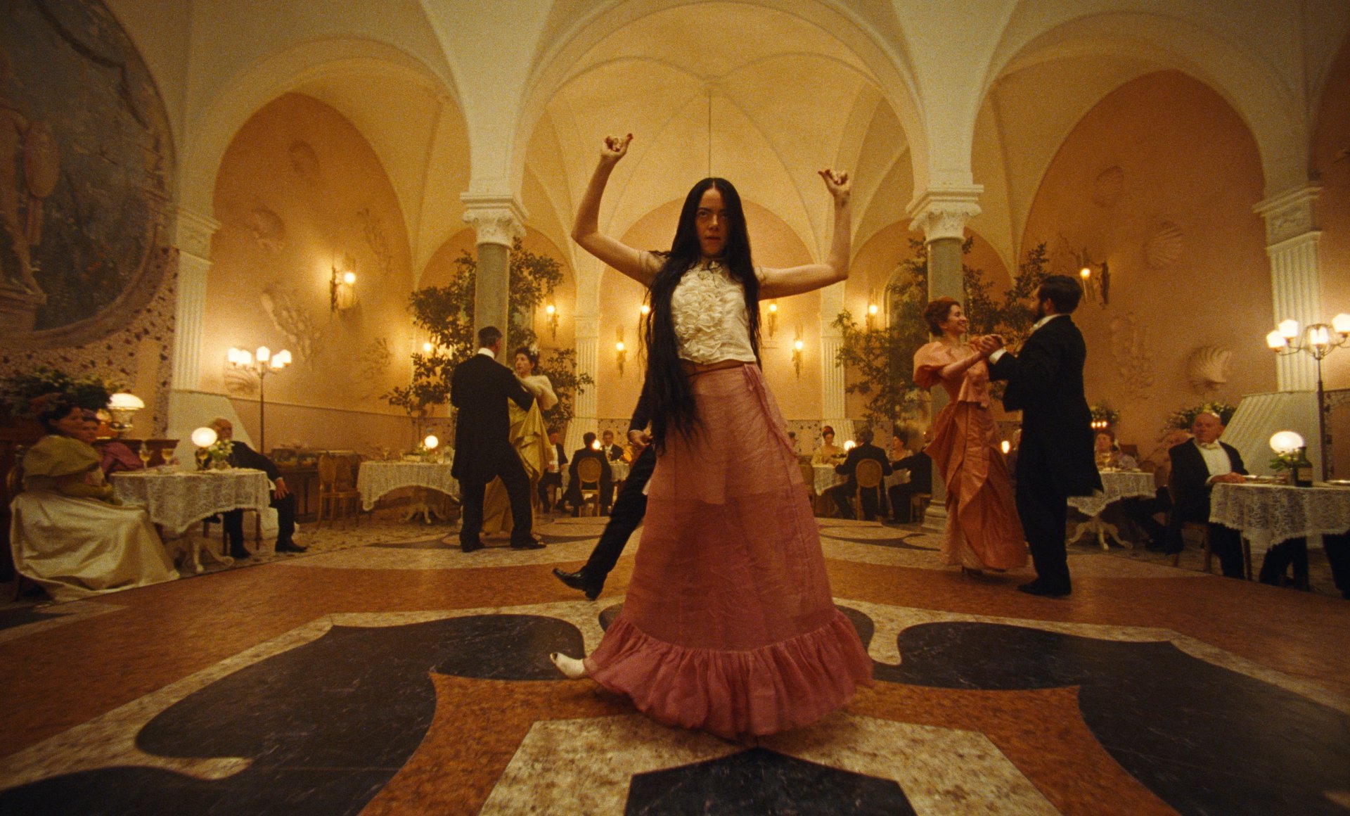 HD wallpaper of a festive ballroom scene from the movie Poor Things with a woman dancing in the foreground.