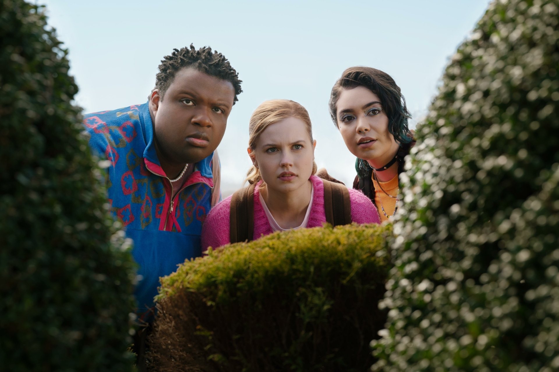 Three characters from Mean Girls (2024) peek through bushes, displaying curious expressions. This image serves as an engaging HD desktop wallpaper and background.