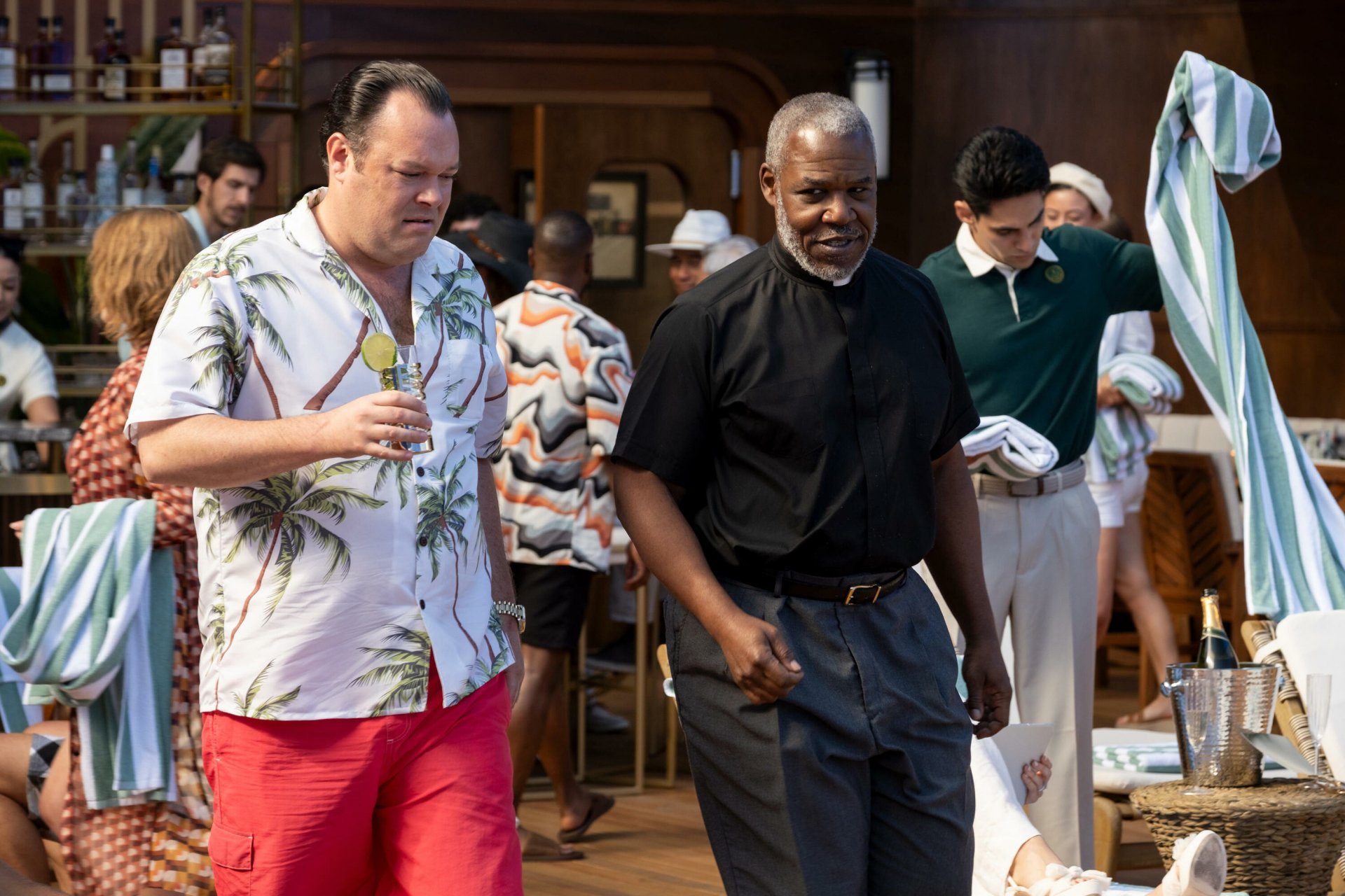 Two actors in a scene from a TV show captured in a high-definition desktop wallpaper, with the setting at a lively venue implied by the background activities and characters' dynamic expressions.