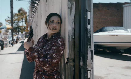 HD wallpaper of a scene from the TV show Griselda (2024) featuring a character cautiously peeking around a corner on a sunny street.