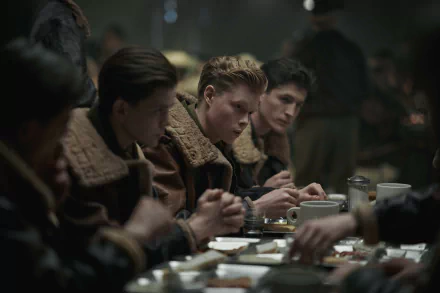 A scene from the TV show *Masters of the Air*, featuring young airmen in vintage uniforms gathered around a dimly lit table, focused on their meal and conversation.