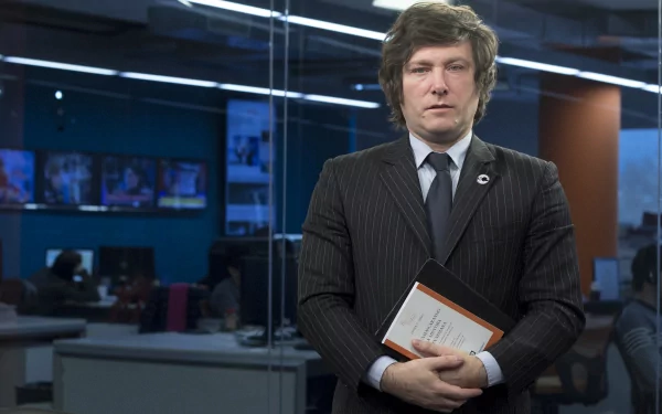 Elegant man in a suit holding a book with a newsroom background for HD desktop wallpaper.