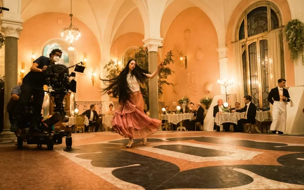 Behind-the-scenes view of an actress dancing during the filming of 'Poor Things' for an elegant HD desktop wallpaper set in a grand ballroom with crew members in the background.