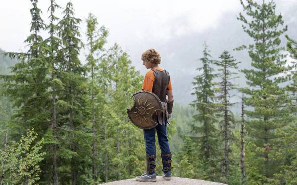 HD wallpaper of a character from Percy Jackson and the Olympians, standing with a shield, overlooking a forest.
