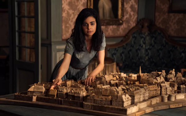 A young woman examines a detailed model of a city in a vintage room, featured in the TV show All the Light We Cannot See. This HD wallpaper captures a moment of intrigue and nostalgia.