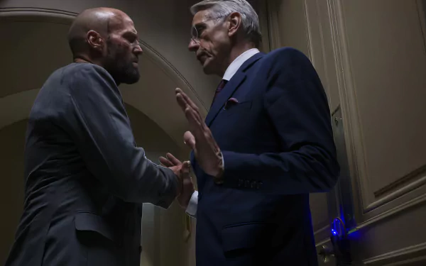HD wallpaper featuring a tense confrontation scene from the movie The Beekeeper, with two men facing each other in a dimly lit corridor.