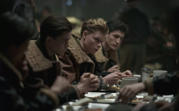 A scene from the TV show *Masters of the Air*, featuring young airmen in vintage uniforms gathered around a dimly lit table, focused on their meal and conversation.