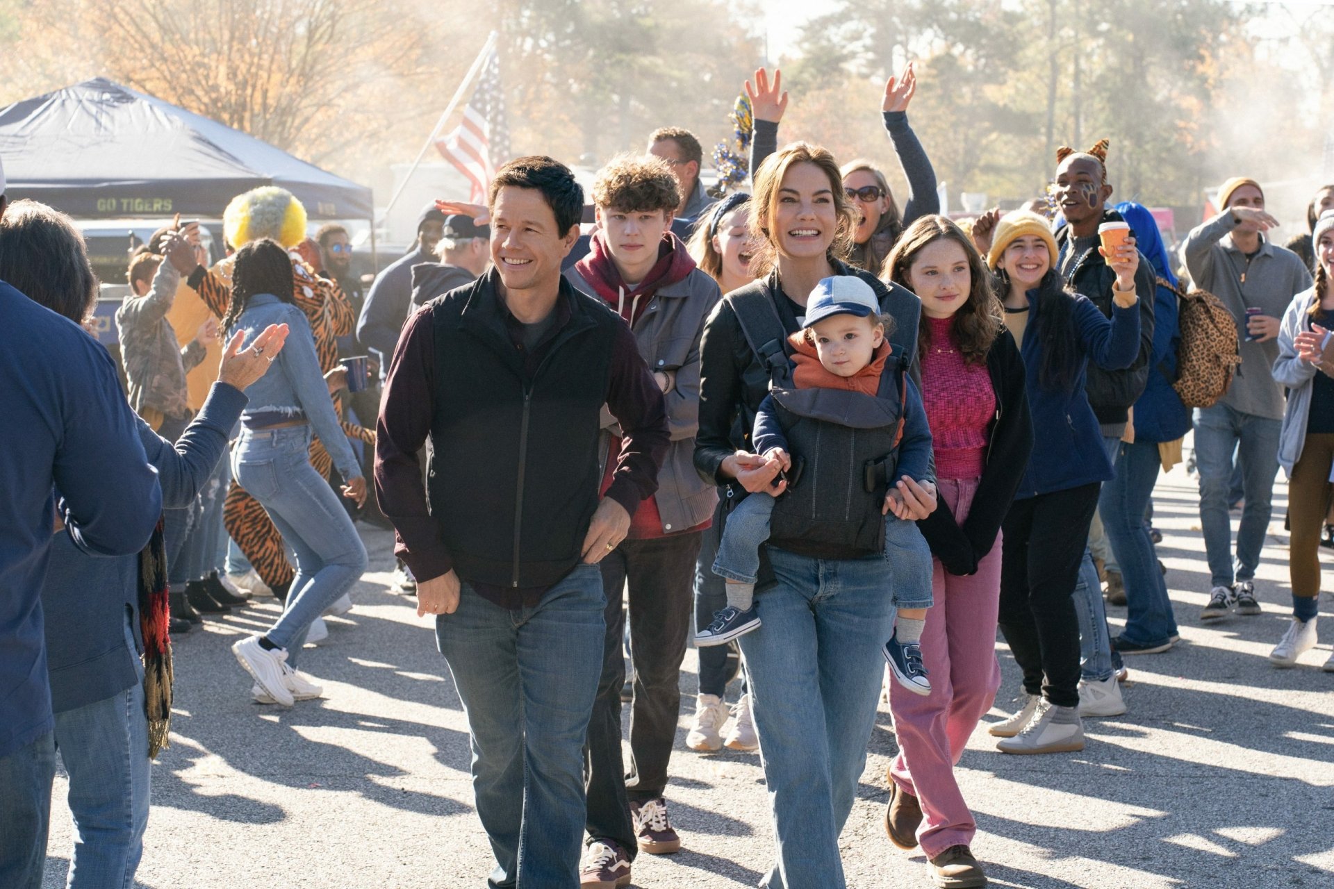 HD desktop wallpaper featuring a scene from the movie The Family Plan with smiling people at an outdoor event.