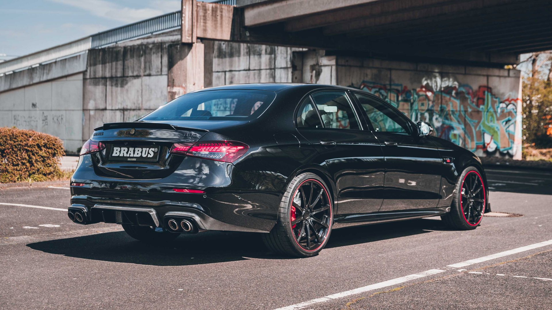 A sleek Brabus 800 E63 parked under a bridge, showcasing its striking design and bold red accents, set against an urban backdrop with graffiti art. HD desktop wallpaper.