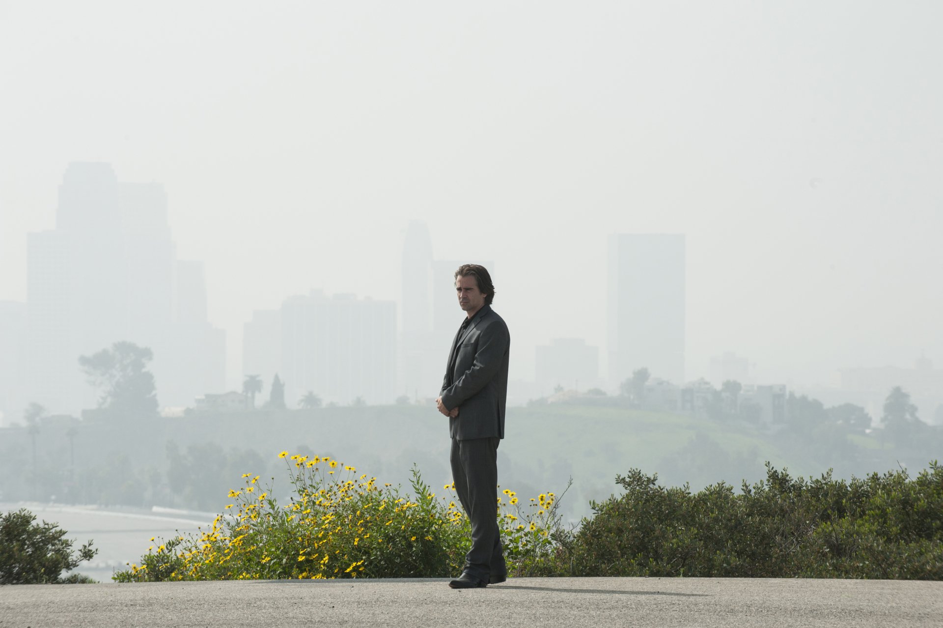 True Detective TV show character standing with a backdrop of a hazy city skyline for an HD desktop wallpaper.