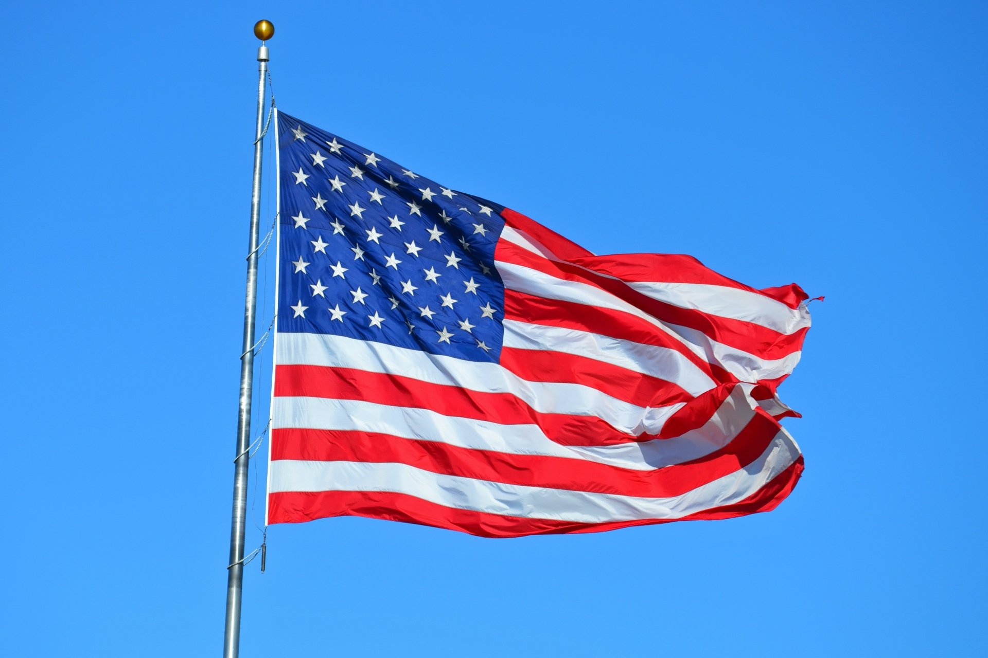 American flag waving against a clear blue sky, available as HD desktop wallpaper and background.