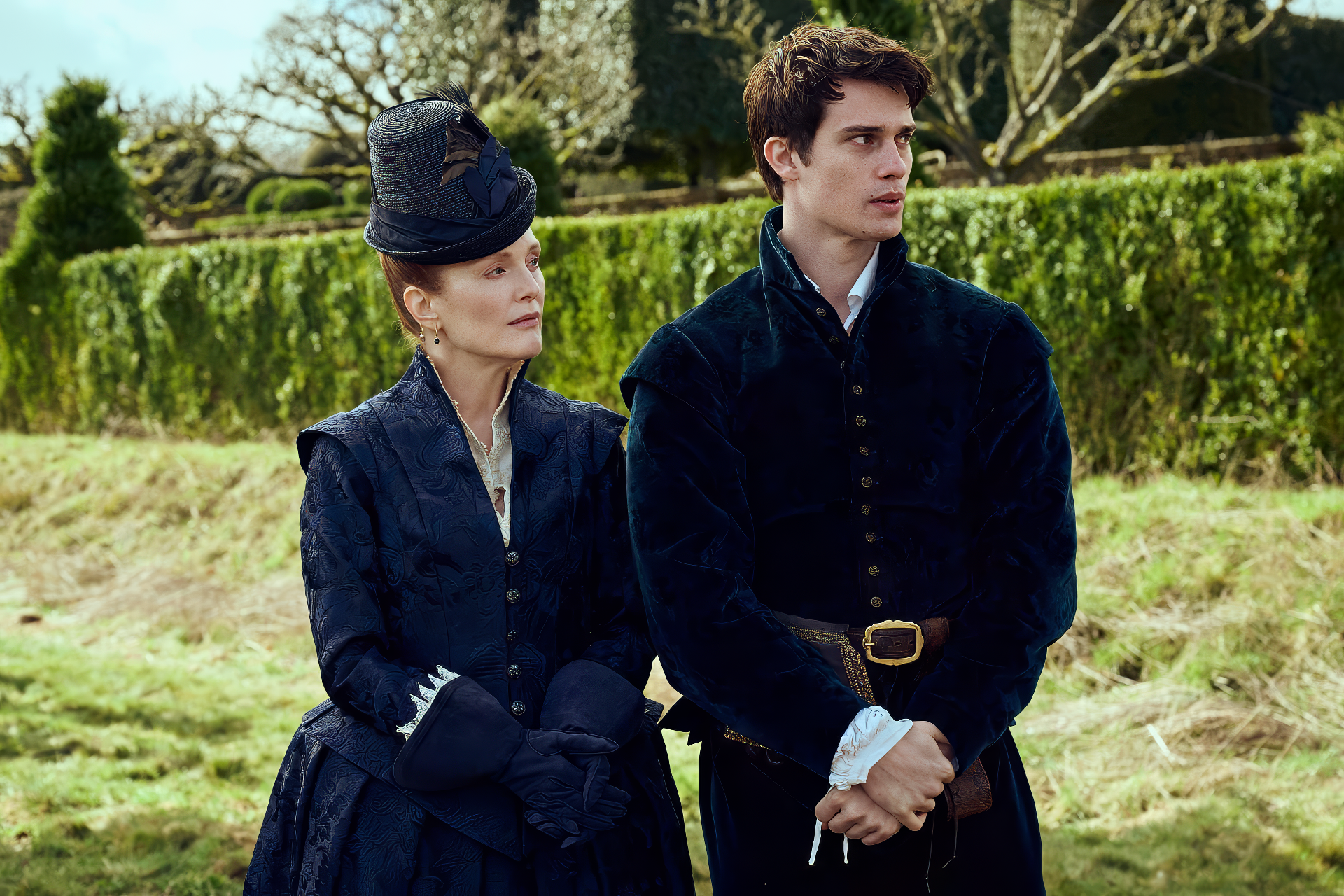 Julianne Moore and Nicholas Galitzine star in Mary & George, captured in a striking HD wallpaper, showcasing their character's historical attire against a scenic backdrop.