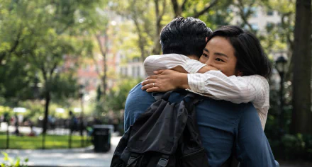 HD wallpaper of a scene from the movie Past Lives featuring two individuals embracing in a heartfelt hug at a park.