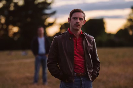 HD desktop wallpaper featuring a contemplative man in the foreground from the movie 'All of Us Are Strangers' with another figure blurred in the background, set in a dusky field.